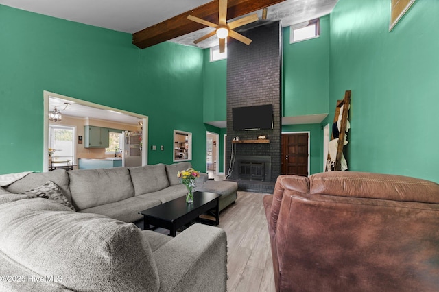 living room with a high ceiling, light wood finished floors, beam ceiling, a wealth of natural light, and a fireplace