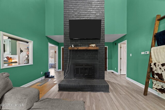 living room featuring baseboards, wood finished floors, a towering ceiling, and a fireplace