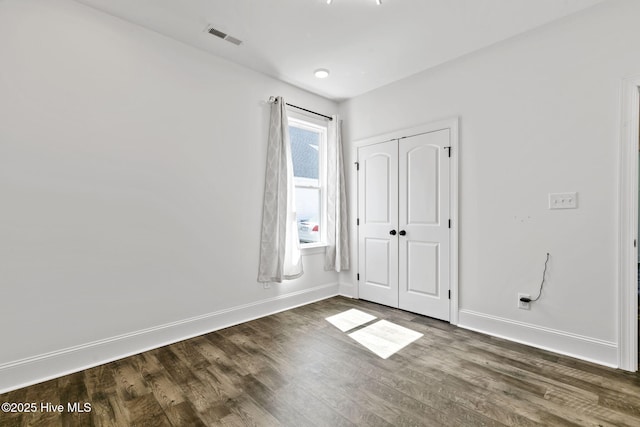 unfurnished bedroom with dark wood-type flooring, a closet, visible vents, and baseboards