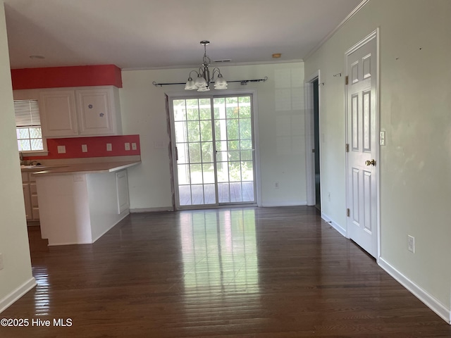 unfurnished dining area with crown molding, a wealth of natural light, dark wood-type flooring, and a notable chandelier