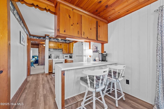 kitchen featuring wood finished floors, brown cabinetry, white appliances, light countertops, and under cabinet range hood