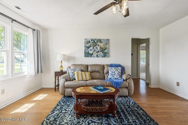 living room featuring light wood-type flooring, a textured ceiling, a ceiling fan, and baseboards