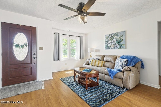 living area with ceiling fan, baseboards, a textured ceiling, and light wood-type flooring