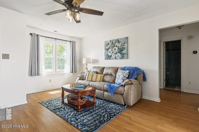 living room with light wood finished floors, a ceiling fan, baseboards, and a textured ceiling