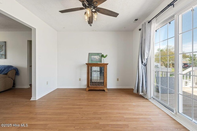 unfurnished living room with light wood-style flooring, a textured ceiling, visible vents, baseboards, and ceiling fan