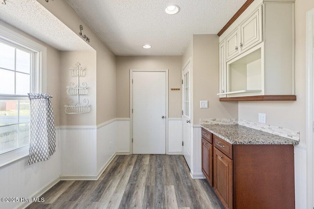 kitchen featuring wood finished floors, a textured ceiling, a wainscoted wall, and light stone counters
