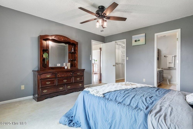 carpeted bedroom with a ceiling fan, a textured ceiling, a walk in closet, connected bathroom, and baseboards