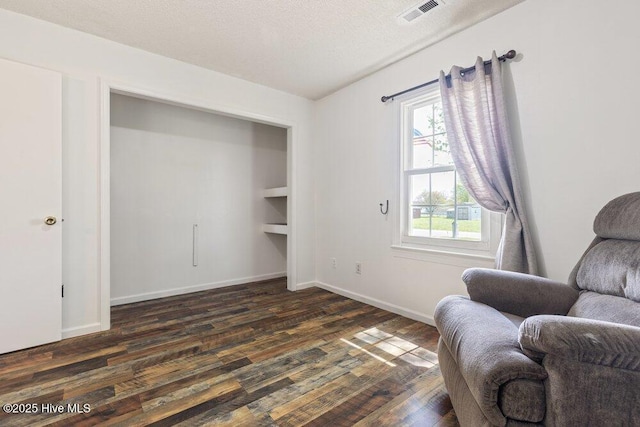 sitting room with a textured ceiling, dark wood finished floors, baseboards, visible vents, and built in shelves