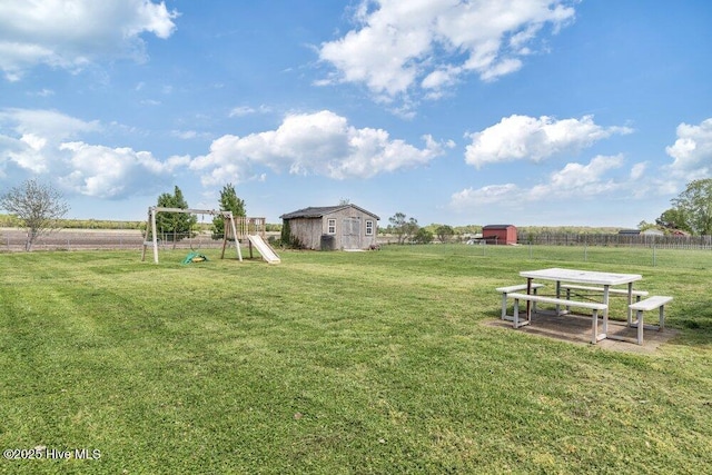 view of yard with an outdoor structure, fence, playground community, and a storage unit
