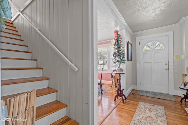 foyer with stairway, wood finished floors, ornamental molding, baseboards, and a textured ceiling