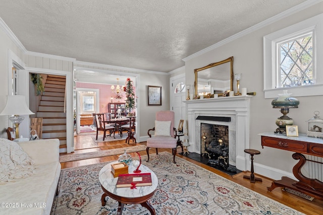 living room with a textured ceiling, a fireplace with raised hearth, wood finished floors, stairway, and crown molding