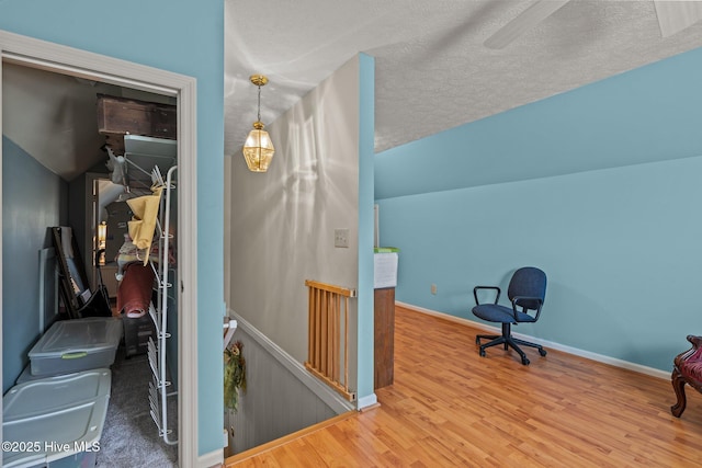 interior space with wood finished floors, a textured ceiling, baseboards, and an upstairs landing