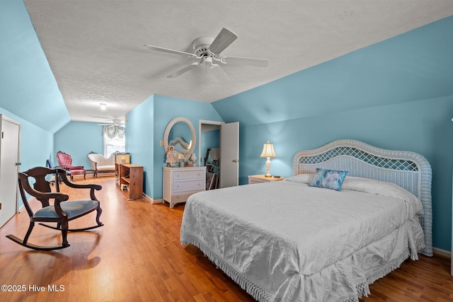 bedroom featuring a textured ceiling, vaulted ceiling, baseboards, wood finished floors, and ceiling fan