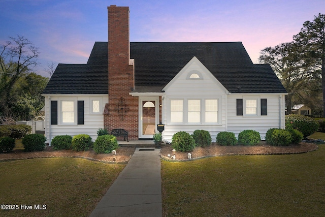 view of front facade featuring a lawn, a chimney, and roof with shingles