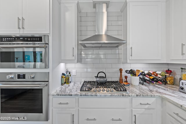 3981 Bay Colony Rd NE, Leland, NC 28451 - kitchen featuring wall chimney exhaust hood, stainless steel appliances, white cabinets, tasteful backsplash, and light stone counters