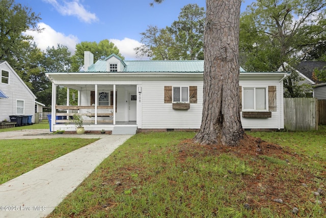 bungalow-style house featuring a front lawn, a porch, a chimney, metal roof, and fence