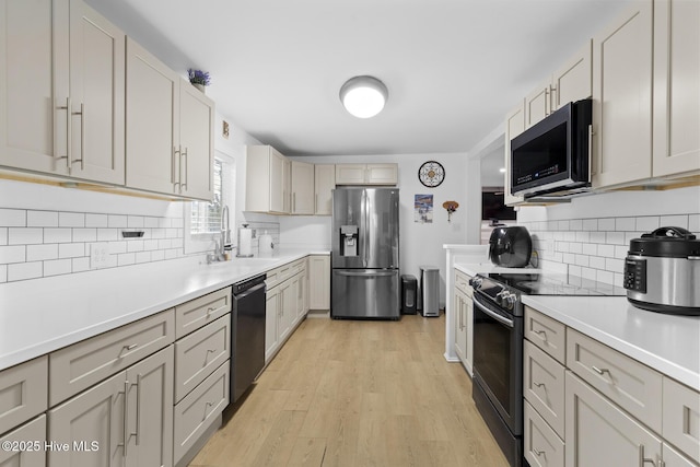 kitchen featuring stainless steel appliances, backsplash, light countertops, a sink, and light wood-style floors