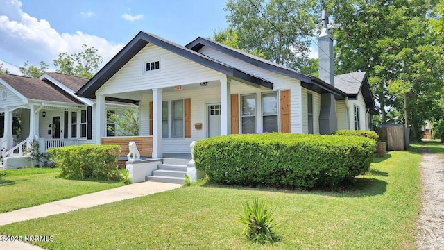 bungalow-style home featuring a chimney, a porch, and a front yard