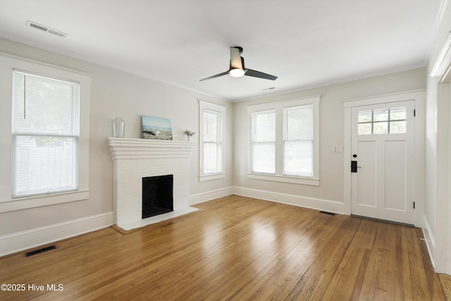 unfurnished living room with a brick fireplace, a ceiling fan, light wood-style flooring, and visible vents