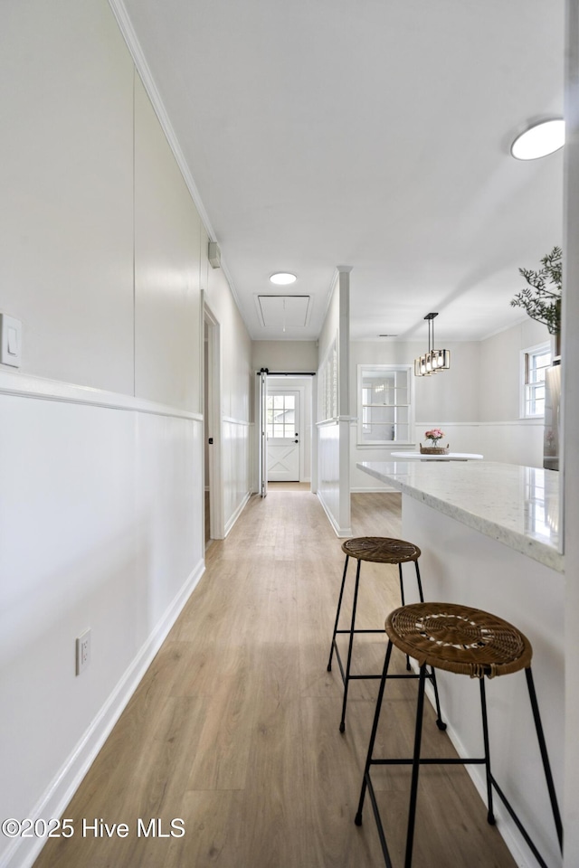 hall with a healthy amount of sunlight, baseboards, light wood-style floors, and attic access