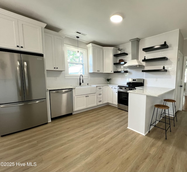 kitchen with visible vents, appliances with stainless steel finishes, open shelves, light wood-type flooring, and wall chimney exhaust hood