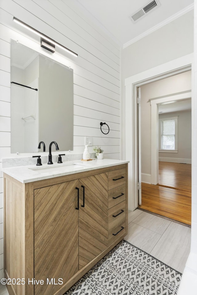 full bath with crown molding, vanity, wood walls, baseboards, and visible vents