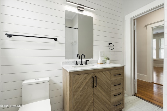 bathroom featuring tile patterned flooring, vanity, toilet, wood walls, and baseboards