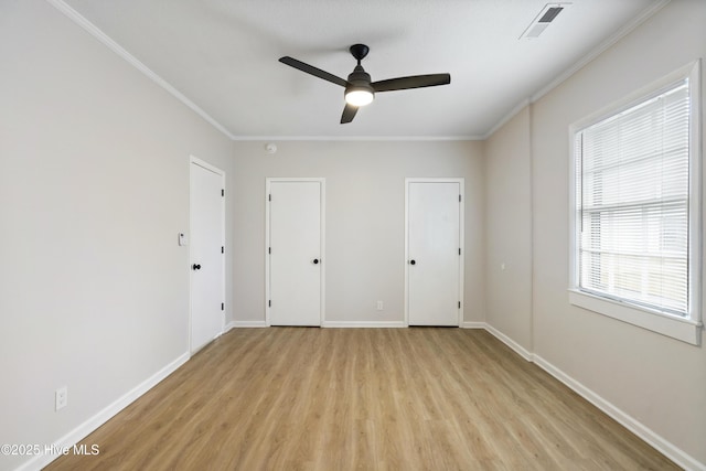 unfurnished bedroom with visible vents, crown molding, baseboards, light wood-style floors, and multiple closets