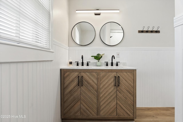 full bath with wood finished floors, a sink, a wainscoted wall, and double vanity