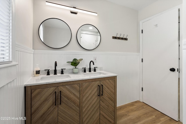 full bathroom with a sink, double vanity, wainscoting, and wood finished floors