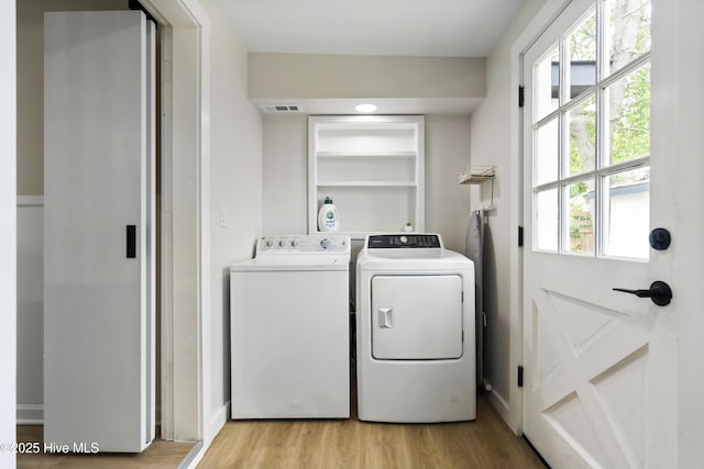 clothes washing area with independent washer and dryer, laundry area, visible vents, and light wood-style flooring