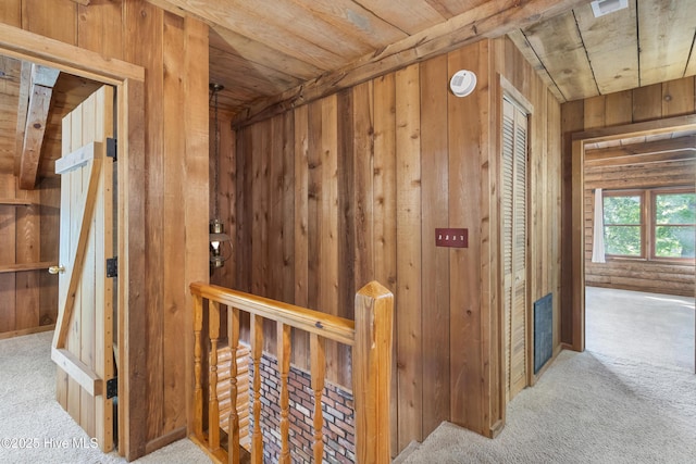 corridor with visible vents, wood walls, carpet, and an upstairs landing