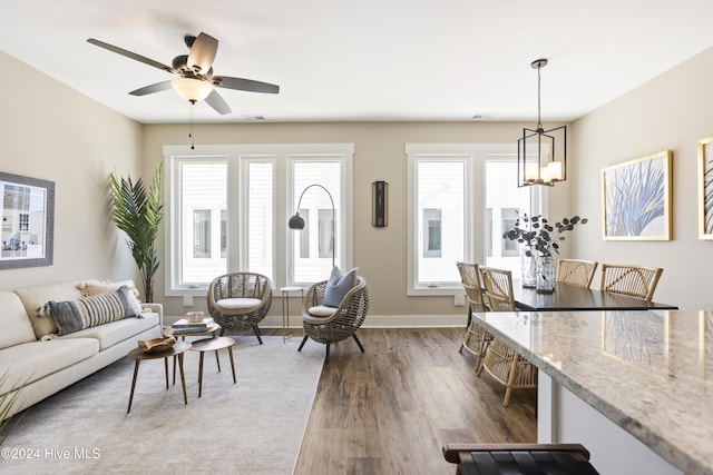 living room with ceiling fan with notable chandelier, baseboards, wood finished floors, and plenty of natural light