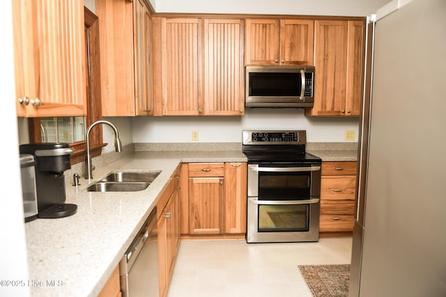 kitchen featuring light floors, light stone counters, a sink, and appliances with stainless steel finishes