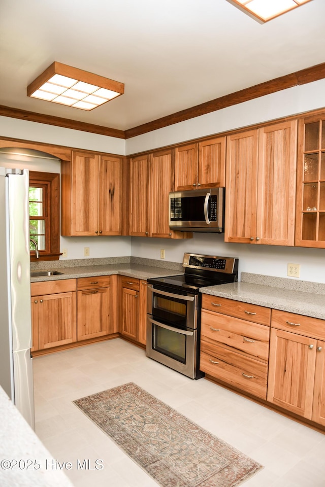 kitchen with light floors, light countertops, a sink, crown molding, and appliances with stainless steel finishes