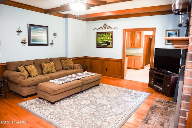 living room featuring beam ceiling, wainscoting, light wood-style floors, a ceiling fan, and wooden walls