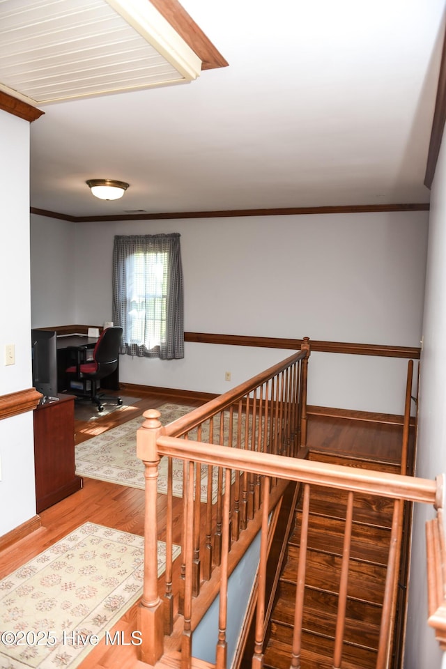 staircase with wood finished floors and ornamental molding