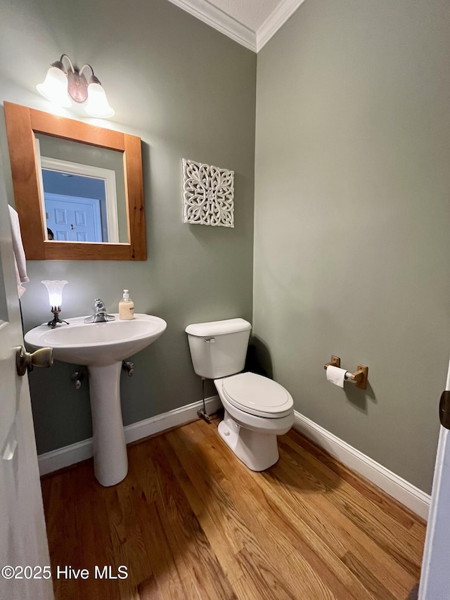 half bathroom with wood finished floors, toilet, baseboards, and ornamental molding