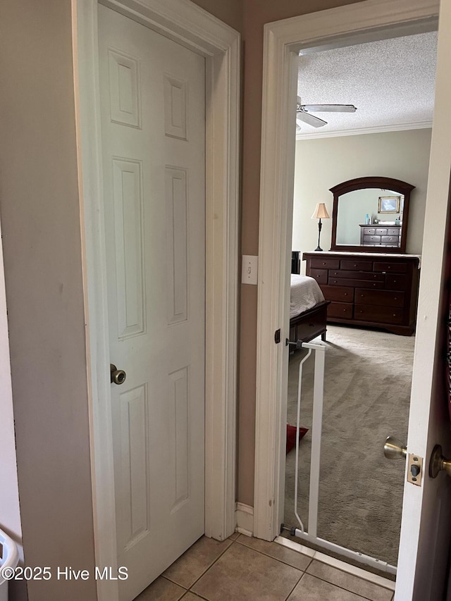 hallway with carpet flooring, tile patterned flooring, a textured ceiling, and ornamental molding