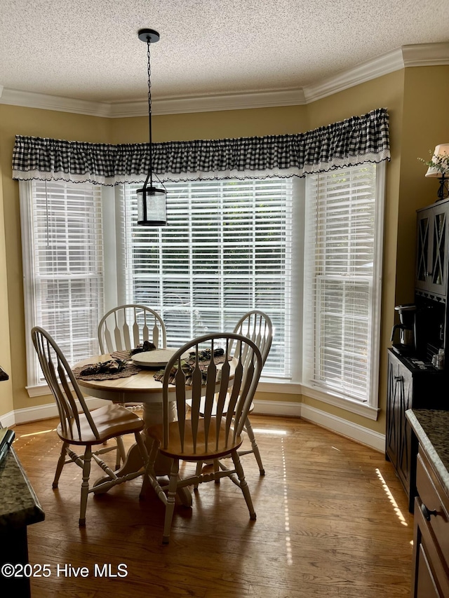 dining room featuring baseboards, crown molding, a textured ceiling, and light wood finished floors
