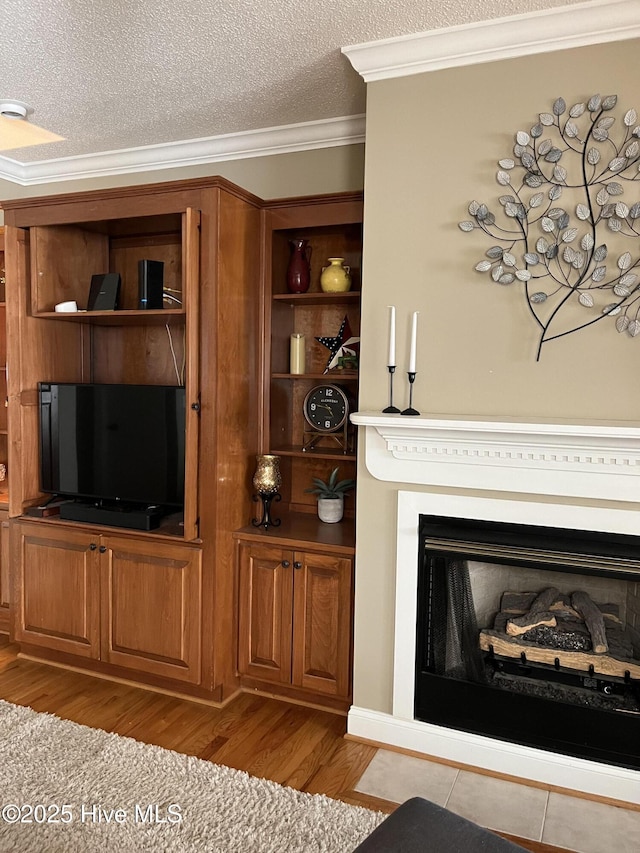 living area with a fireplace, wood finished floors, a textured ceiling, and crown molding