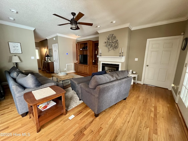 living room with visible vents, ornamental molding, light wood-style floors, a fireplace, and ceiling fan