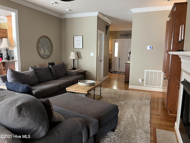 living area with a fireplace with flush hearth, light wood-style flooring, baseboards, ornamental molding, and visible vents
