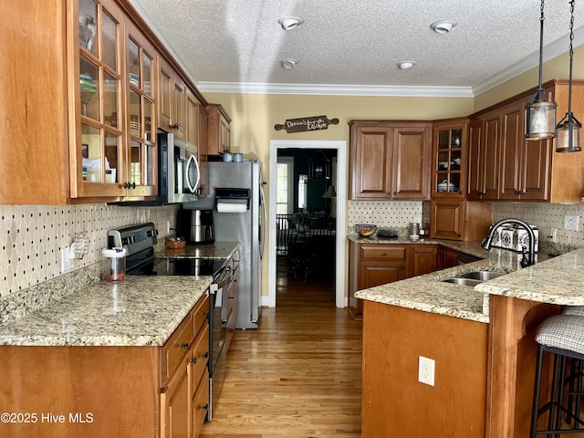 kitchen featuring brown cabinets, a kitchen breakfast bar, stainless steel appliances, a sink, and light stone countertops