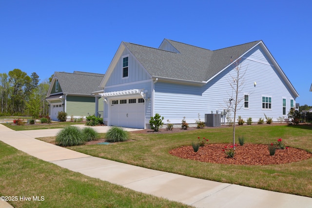 3347 Island Lakes Dr, Oak Island, NC 28461 - view of property exterior featuring central AC, a garage, a shingled roof, board and batten siding, and a yard