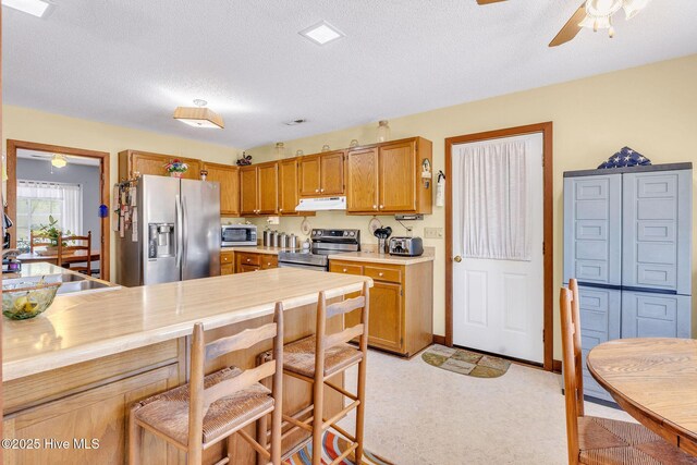 3421 Bethel Rd, Wilmington, NC 28409 - kitchen with under cabinet range hood, light countertops, a ceiling fan, a textured ceiling, and appliances with stainless steel finishes