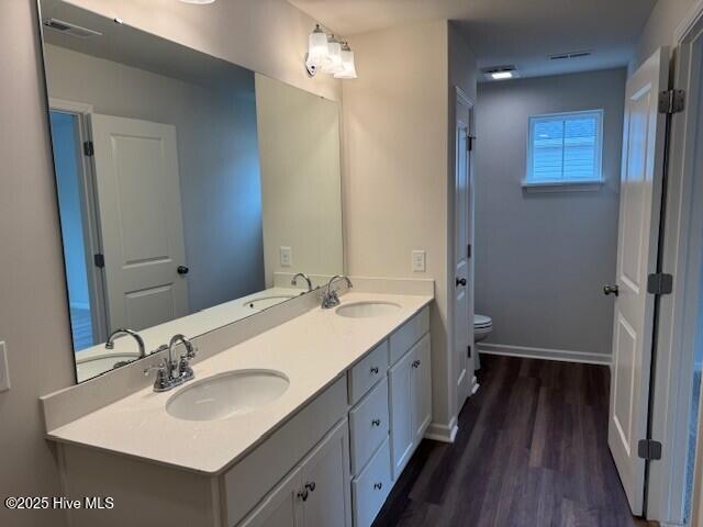 full bathroom featuring toilet, wood finished floors, double vanity, and baseboards