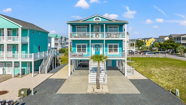 raised beach house featuring a balcony, driveway, a carport, a front yard, and a residential view