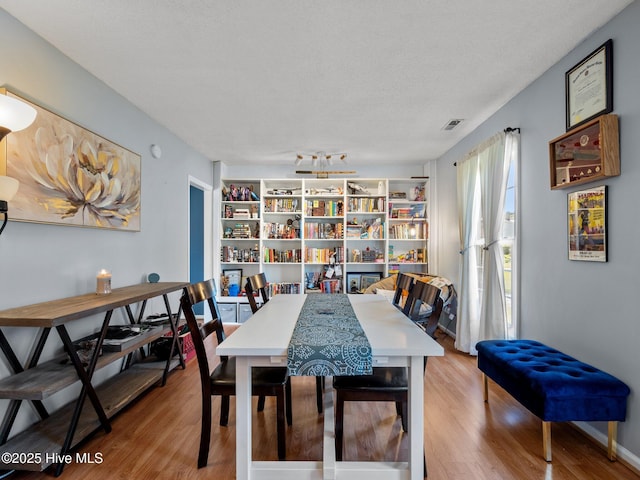 dining area featuring a textured ceiling, wood finished floors, and visible vents