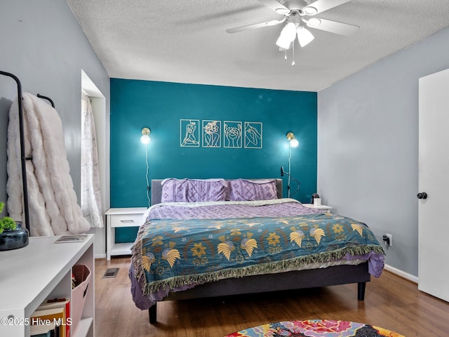 bedroom with a textured ceiling, visible vents, baseboards, wood finished floors, and ceiling fan